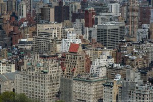 Здание с красной крышей — это 825 Fifth Avenue. 23-этажный бывший апартмент-отель 1926 года постройки. Их строили по всей Америке, но особенной популярностью подобный тип зданий пользовался в Нью-Йорке. Из-за отсутствия кухонь (по концепции жильцы питались в ресторане отеля) подобные здания не попадали под ограничение высотности жилых многоквартирных домов в соответствии с Жилищным актом 1901 года (не выше 45 метров), имели меньше требований по пожарной безопасности и еще несколько послаблений, упрощавших их постройку. Но после сдачи дома жильцы сами тайно устанавливали кухни и жили в полноценных квартирах.